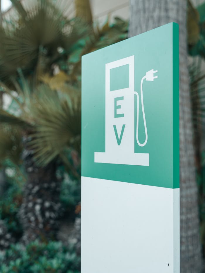 Close-up of a green and white electric vehicle charging station sign with nature background.